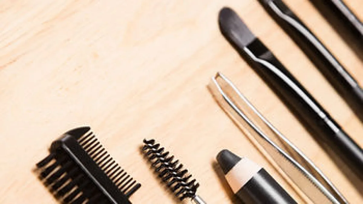 Close-up of eyebrow/beauty tools arranged on a light wood surface.