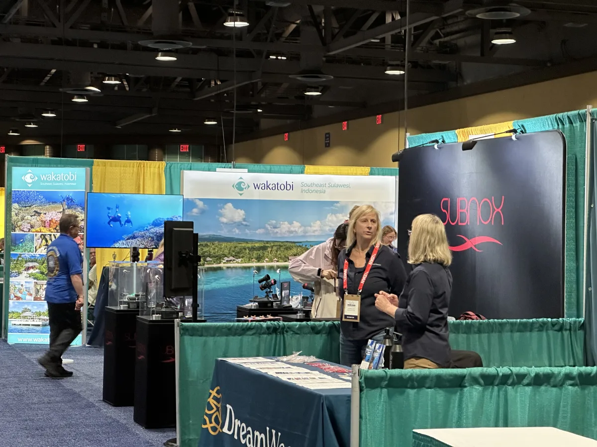 Indoor expo/trade-show floor with multiple exhibition booths separated by green/yellow drapes.