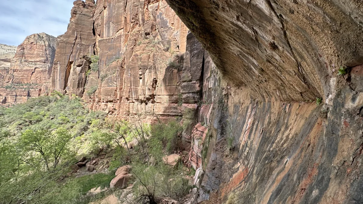 Wide landscape view of a rugged canyon with tall, layered sandstone cliffs.