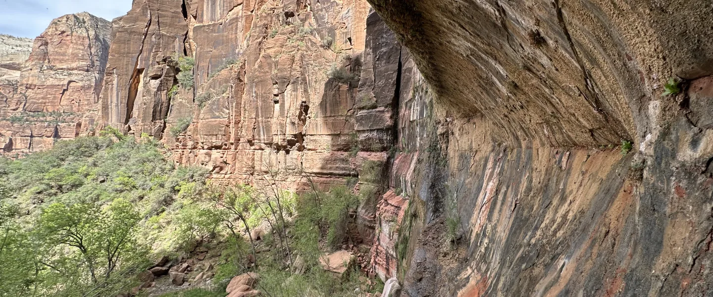 Wide landscape view of a rugged canyon with tall, layered sandstone cliffs.