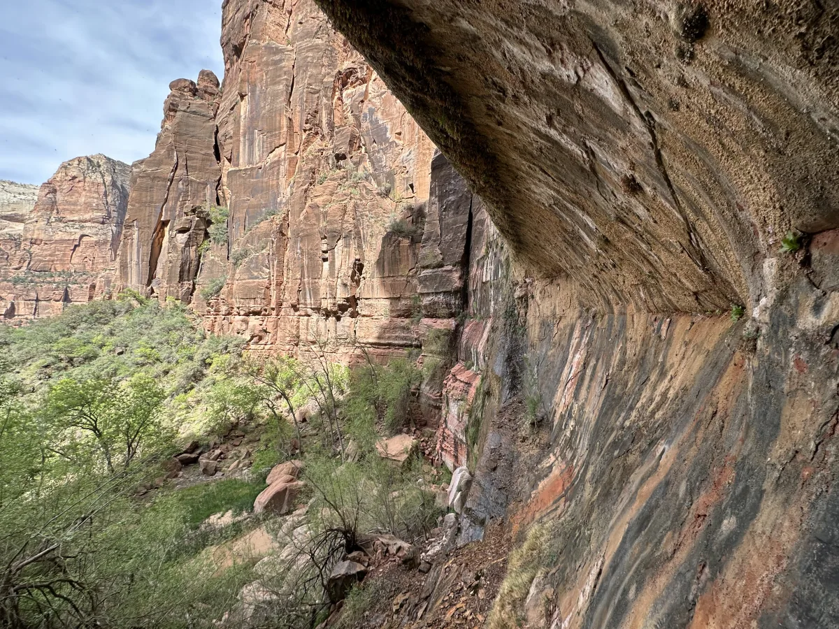 Wide landscape view of a rugged canyon with tall, layered sandstone cliffs.