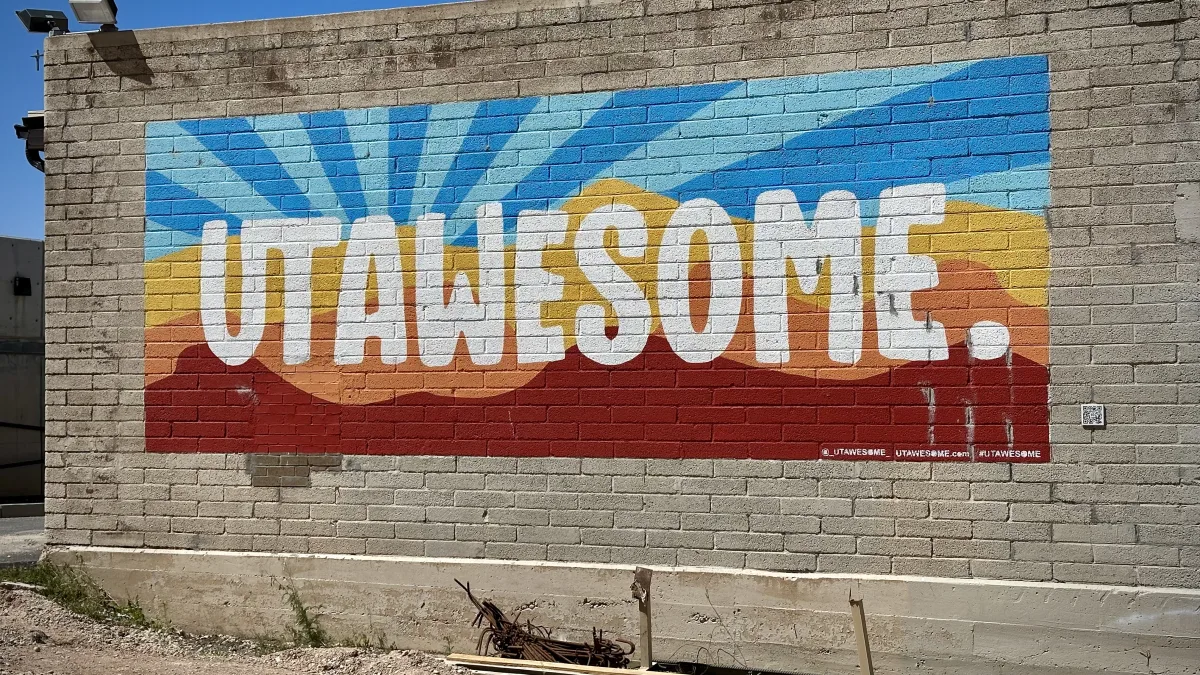 Outdoor photo of a large painted mural on a gray brick wall.