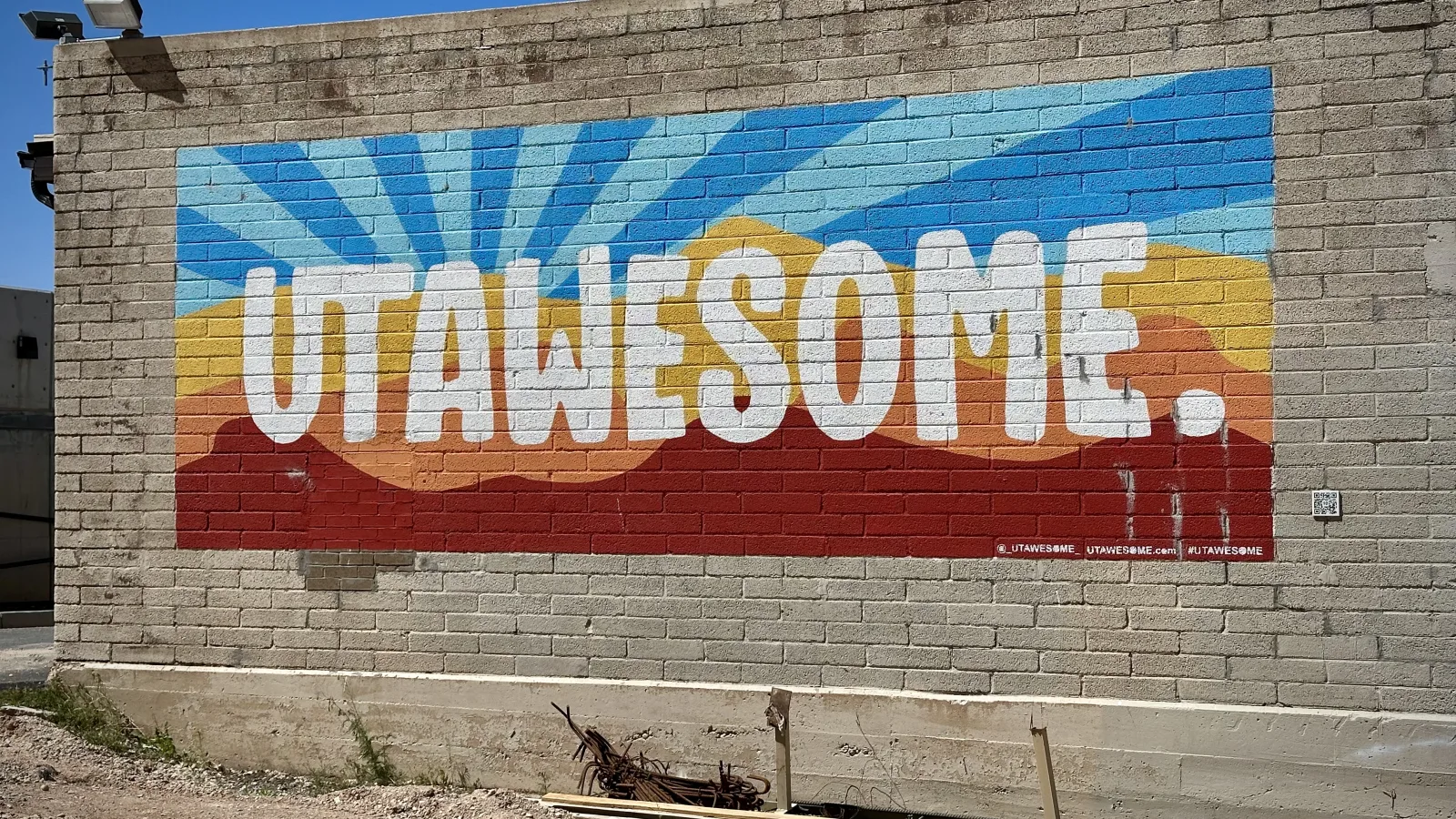 Outdoor photo of a large painted mural on a gray brick wall.